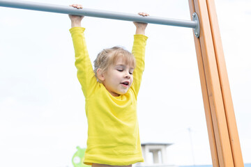 Child playing on outdoor playground. Kids play on school or kindergarten yard. Active kid on horizontal bar. Healthy summer activity for children. Little girl climbing.
