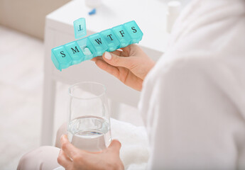 Woman with pill box and water in glass at home, closeup