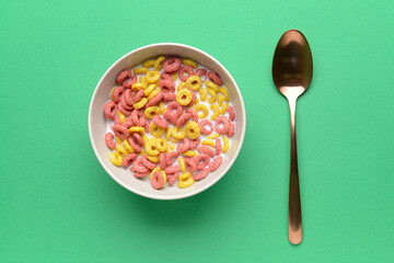 Bowl with crunchy corn flakes rings and milk on color background