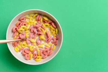 Bowl with crunchy corn flakes rings and milk on color background