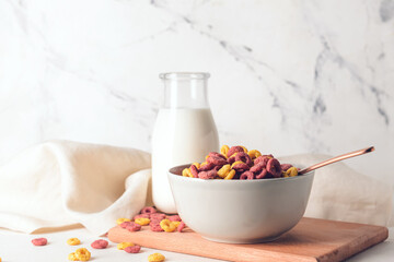 Bowl with crunchy corn flakes rings and bottle of milk on light background