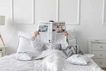 Morning of young woman reading newspaper in bed