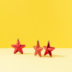 Three red stars Christmas ornaments against yellow background. Minimal New Year celebration concept. Sunlight shadows.