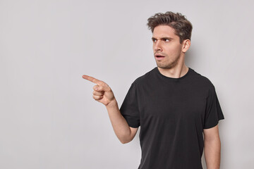 Horizontal shot of angry young European man points index finger away shows copy space for your...