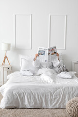 Morning of young woman reading newspaper in bed