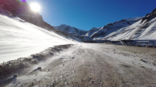 Wind and snowstorm blows strongly from the mountain with sunlight. Snowstorm high in the mountains. High-mountain mudflow protection dam Mynzhylki, Kazakhstan.