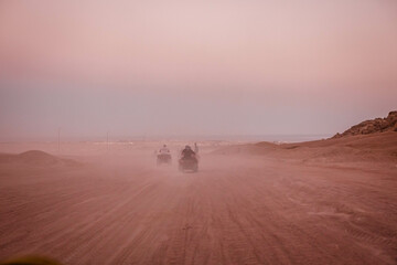 Group of tourist on ATVs on Egyptian desert. A lot of quad bikes in the dust ride on the background of the wild desert. Sunset in the desert beyond the mountains. ATV rally. © popovatetiana