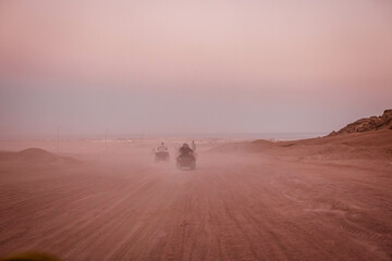 Group of tourist on ATVs on Egyptian desert. A lot of quad bikes in the dust ride on the background of the wild desert. Sunset in the desert beyond the mountains. ATV rally.