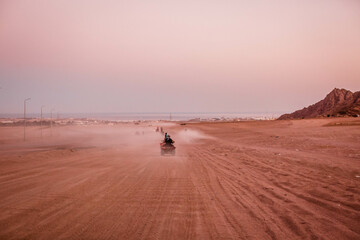 Group of tourist on ATVs on Egyptian desert. A lot of quad bikes in the dust ride on the background of the wild desert. Sunset in the desert beyond the mountains. ATV rally.