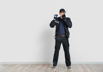 Young policeman with two-way radio and flashlight near light wall