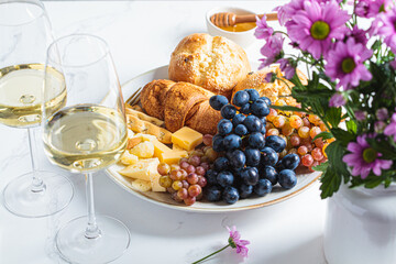 Valentine's day date. Cheese with fruits and buns with glasses of white wine on table with flowers.