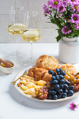 Valentine's day date. Cheese with fruits and buns with glasses of white wine on table with flowers.