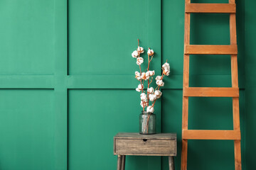 Vase with beautiful cotton flowers on table near color wall