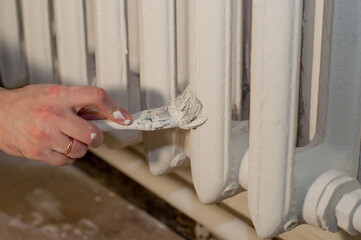 a man's hand with a ring paints the battery with a white paint brush
