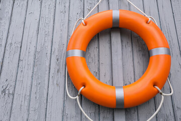 Orange life buoy hanging on light wooden wall, space for text