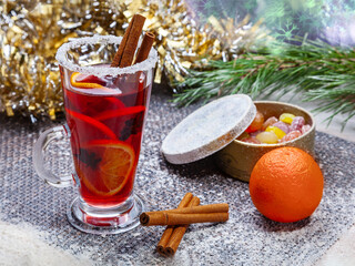 Christmas hot mulled wine with a slice of orange and spices. A glass cup with a hot traditional drink on a snowy background in festive decorations. Evening mood and decoration 