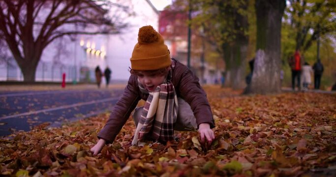 Delighted Kid Having Fun Grabbing And Throwing The Fallen Leaves In The Autumn City