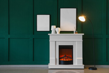Fireplace with vases, glowing lamp and blank frames hanging on green wall