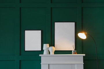 Fireplace with vases, glowing lamp and blank frames hanging on green wall