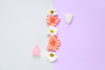 Menstrual cups and flowers on color background