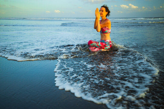 Beach yoga. Attractive woman practicing Gomukhasana Garudasana. Cow Face Pose with Eagle Arms. Waves on black sand. Slim fit body. Zen life. Self care concept. Yoga retreat. Copy space. Bali