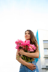 A young caucasian woman holding a bouquet of bright colors, a girl in denim shorts in summer with bunch of flowers , a lady in summer clothes against the sky