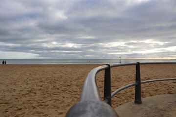 black metal railings looking onto a yellow sandy beach and cloudy Autumn sky