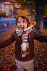 delighted young boy having fun on a walk in autumn city, throwing and catching fallen leaves