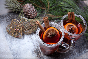 Christmas hot mulled wine with a slice of orange and spices. A glass cup with a hot traditional drink on a snowy background in festive decorations. Evening mood and decoration 