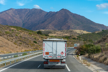 Truck transporting solid dangerous goods in bulk driving on the highway, rear view.