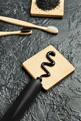 Activated charcoal tooth powder, toothpaste tube and bamboo toothbrushes on dark background, closeup