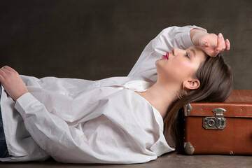 A beautiful girl lies on an old suitcase on a gray background.