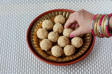Til ladoo laddu woman hand take white sesame ladoo ellu urundai Indian festival food snack sweet Lohri Makar Sankranti Pongal Diwali harvest festival Tamil Nadu winter festival Punjab North India 