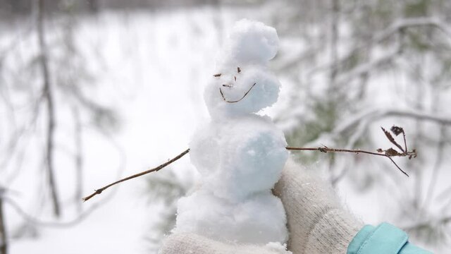 A small cute snowman on the background of a snow-covered fir tree in the hands of a man.