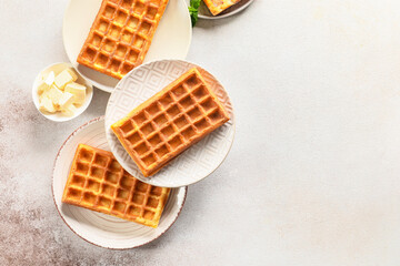 Plates with delicious Belgian waffles and butter on light background