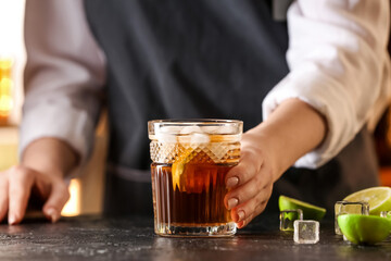 Female bartender with glass of tasty Cuba Libre cocktail on table in bar