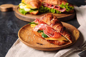 Plate of delicious croissant sandwich with meat and cheese on black background