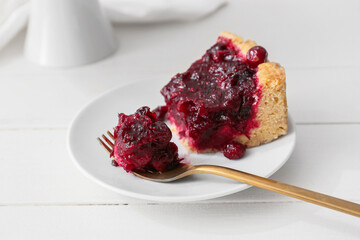 Plate with piece of delicious lingonberry pie on light wooden background, closeup