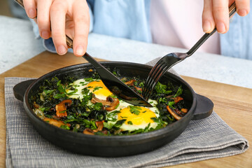 Woman eating tasty Shakshouka at kitchen table