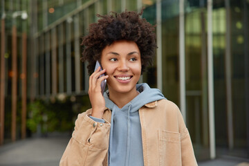 Modern technologies and people concept. Happy young curly haired woman enjoys cellular...