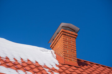 Red roof of a detached house and chimney and snow against the blue sky in winter