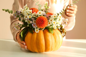Female florist making beautiful autumn bouquet in pumpkin on table