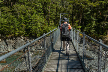 Hikers walking on a swing bridge at Roueturn Track, one of the Great Walks of New Zealand.