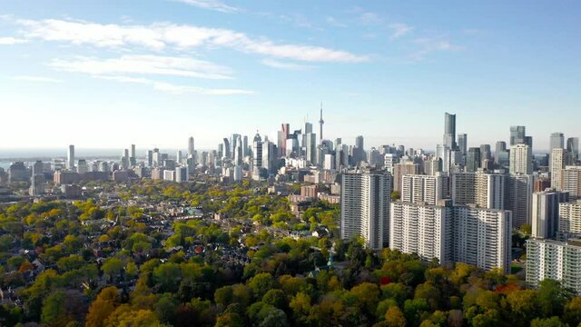A drone view of downtown Toronto captures Riverdale East Park's vibrant fall colors&mdash;red, green, orange, and yellow. The iconic Toronto skyline features the city's tallest structure against a blue sky 