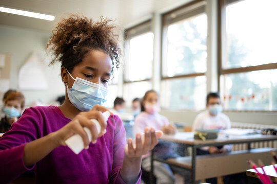 School children wearing face masks and disinfecting their hands in classroom during corona virus pandemic.