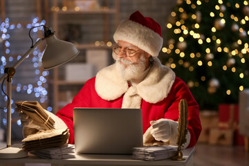 Santa Claus with laptop and letters at home on Christmas eve