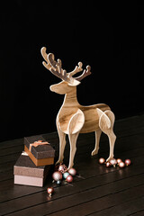 Wooden reindeer, Christmas balls and gift boxes near dark wall