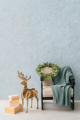 Wooden reindeer, gift boxes and armchair with plaid and Christmas wreath near color wall