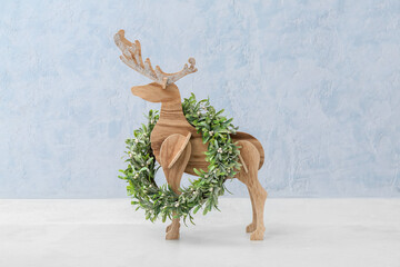 Wooden reindeer with Christmas wreath on color background