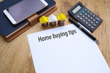 Home buying tips was written on white paper with house model from stacked coins, pen, calculator,...